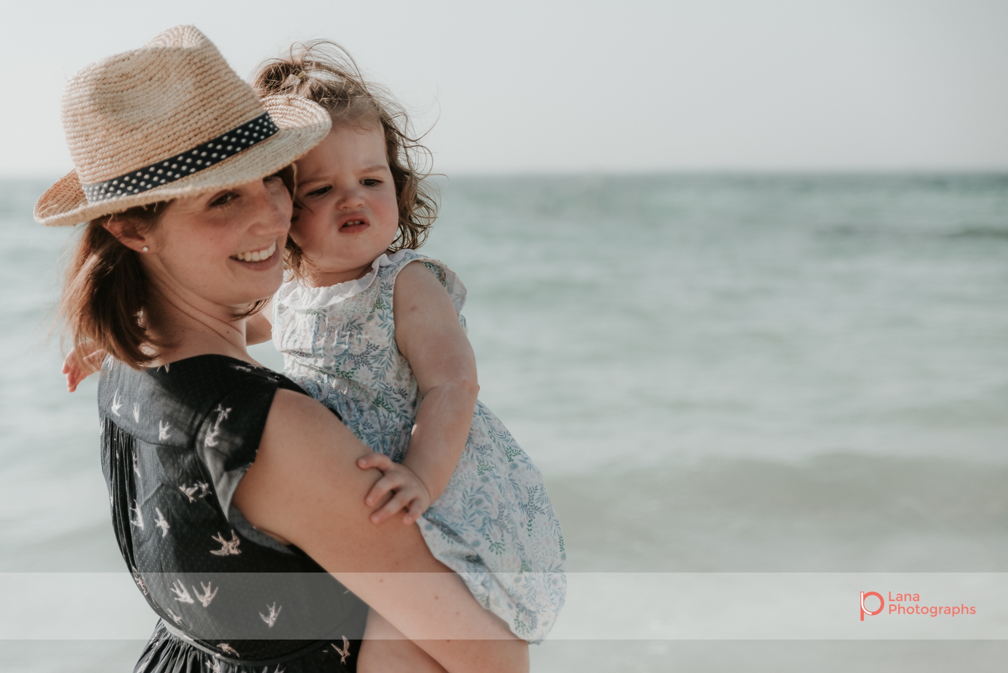 Lana Photographs Maternity Photography Dubai Professional Maternity Photographer mother in a hat carrying her little girl by the beach