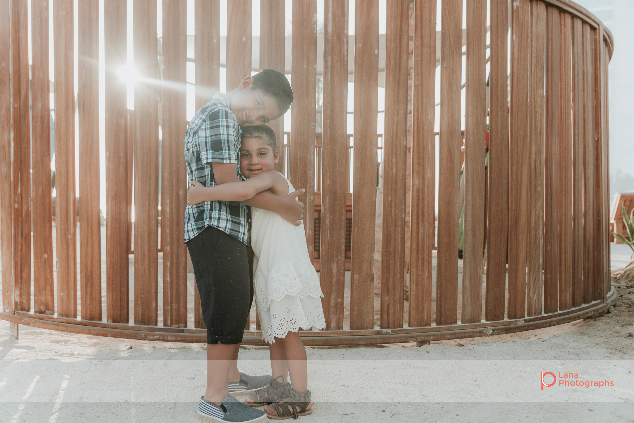  Lana Photographs Dubai Family Photography beach photoshoot portrait of brother and sister hugging with sun flare  