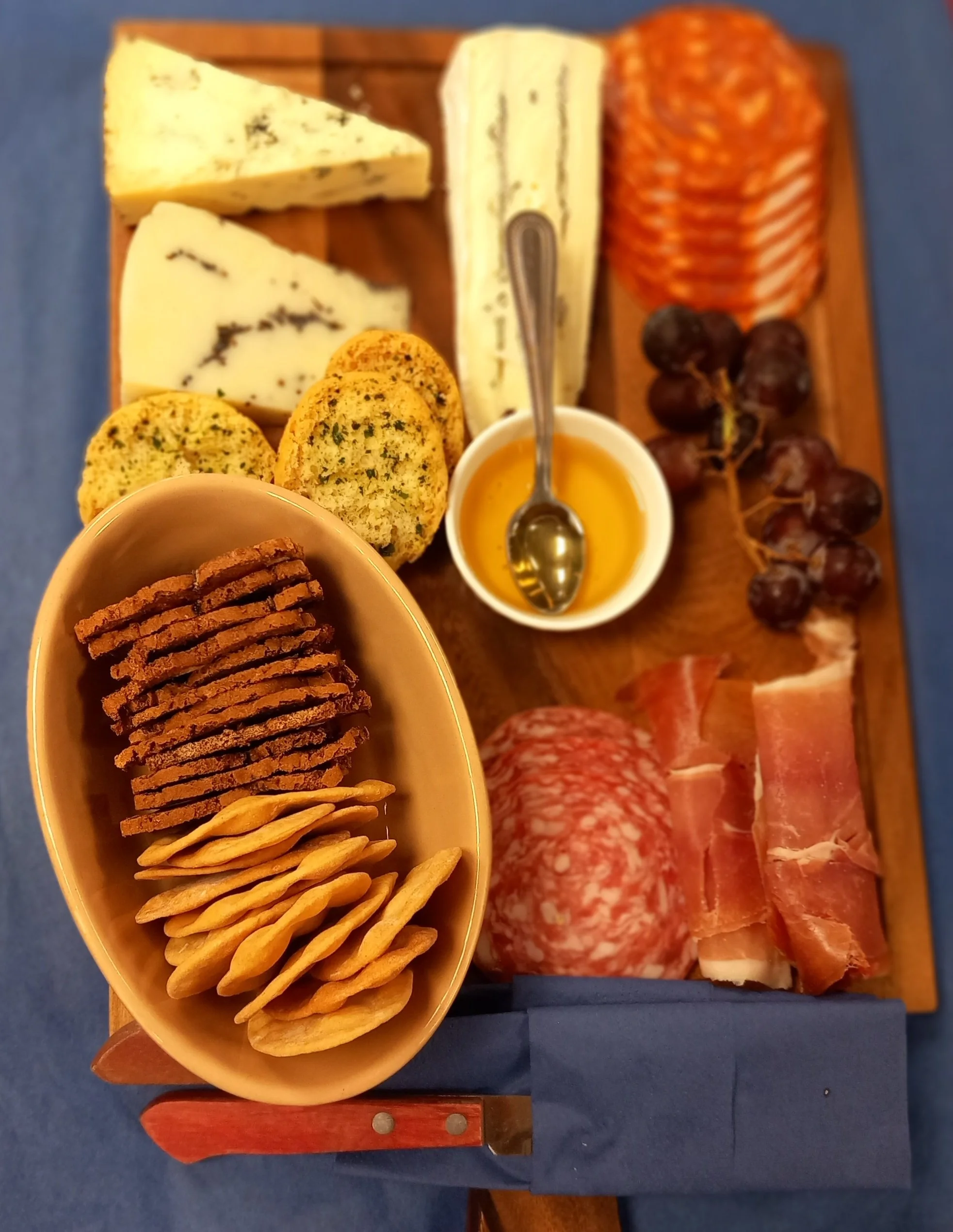 Charcuterie board with assorted cheeses, cured meats, grapes, crackers, and honey.