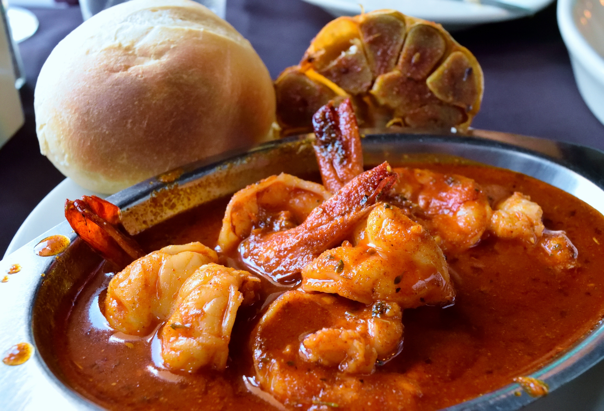 NOLA BBQ Shrimp with a roll and a fresh head of garlic.