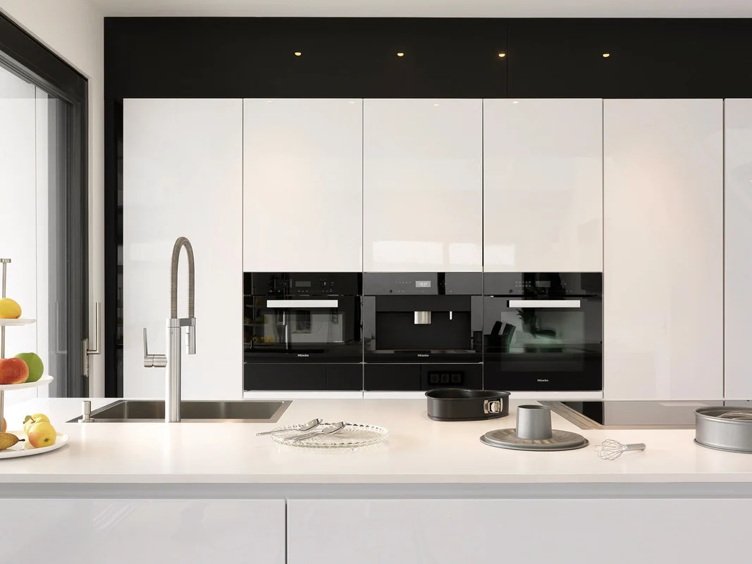 The kitchen is at the heart of the house, immediately adjacent to the covered veranda. The transition into the living room area is fluid and accentuated by a step. The kitchen is kept very minimalist with a food preparation island opposite the wall unit with handle-less, high-gloss fronts. 