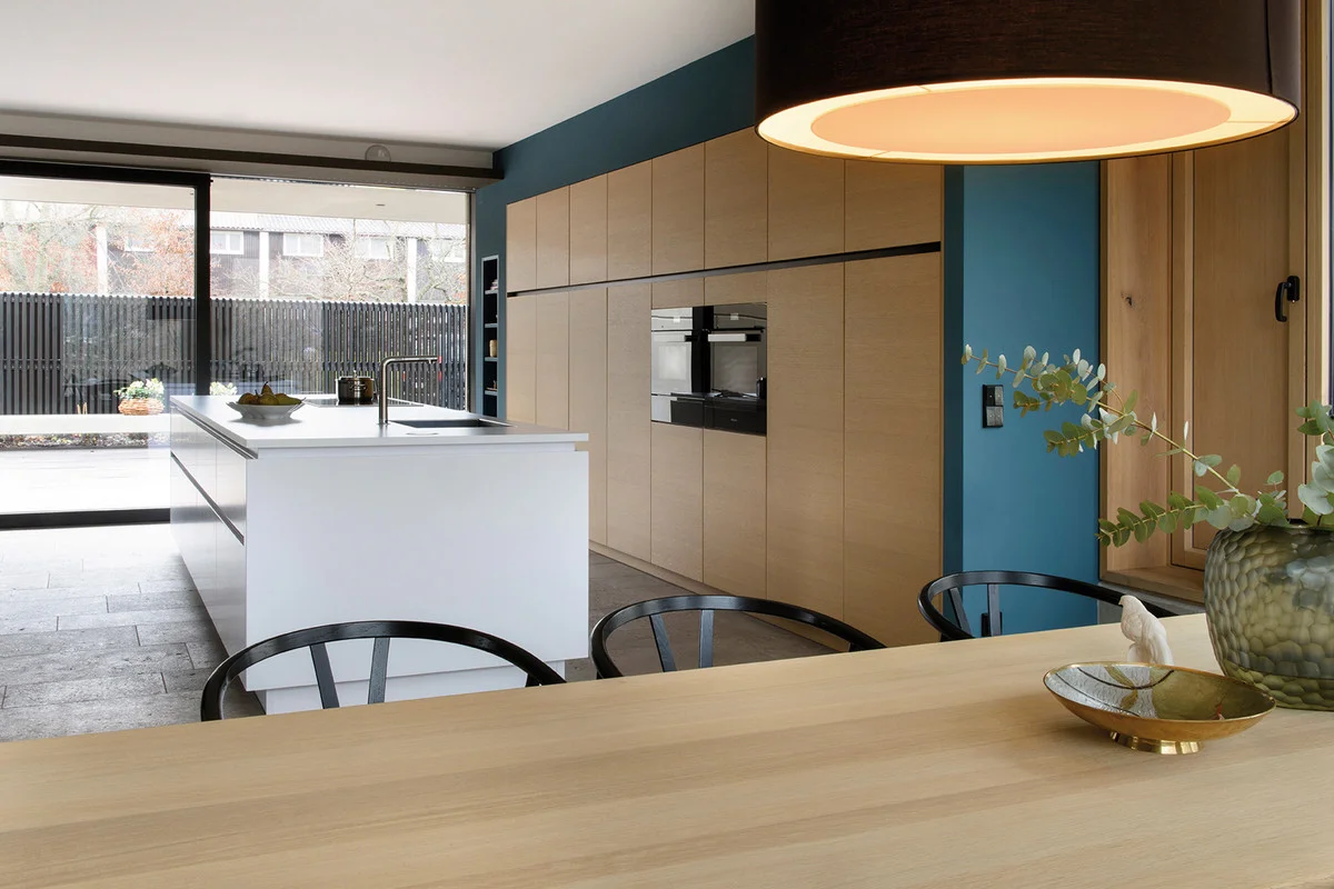 The kitchen is spacious and opens onto the living area. The virtually floor-to-ceiling unit run is custom-fit into a niche and has a very homely look with its genuine oak front. It is an exciting contrast to the blue on the walls and the high-gloss white of the kitchen island. 