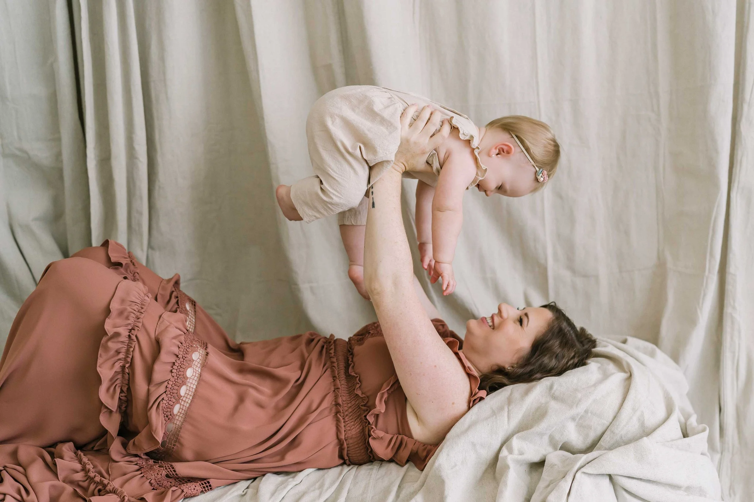 Mom lying back and lifting her laughing baby girl into the air during a first year session in Grimsby