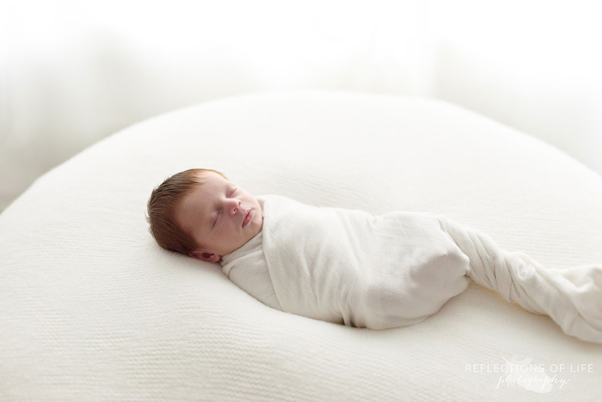 011 newborn baby boy wrapped in white on large white pillow in Ontario Canada photo studio