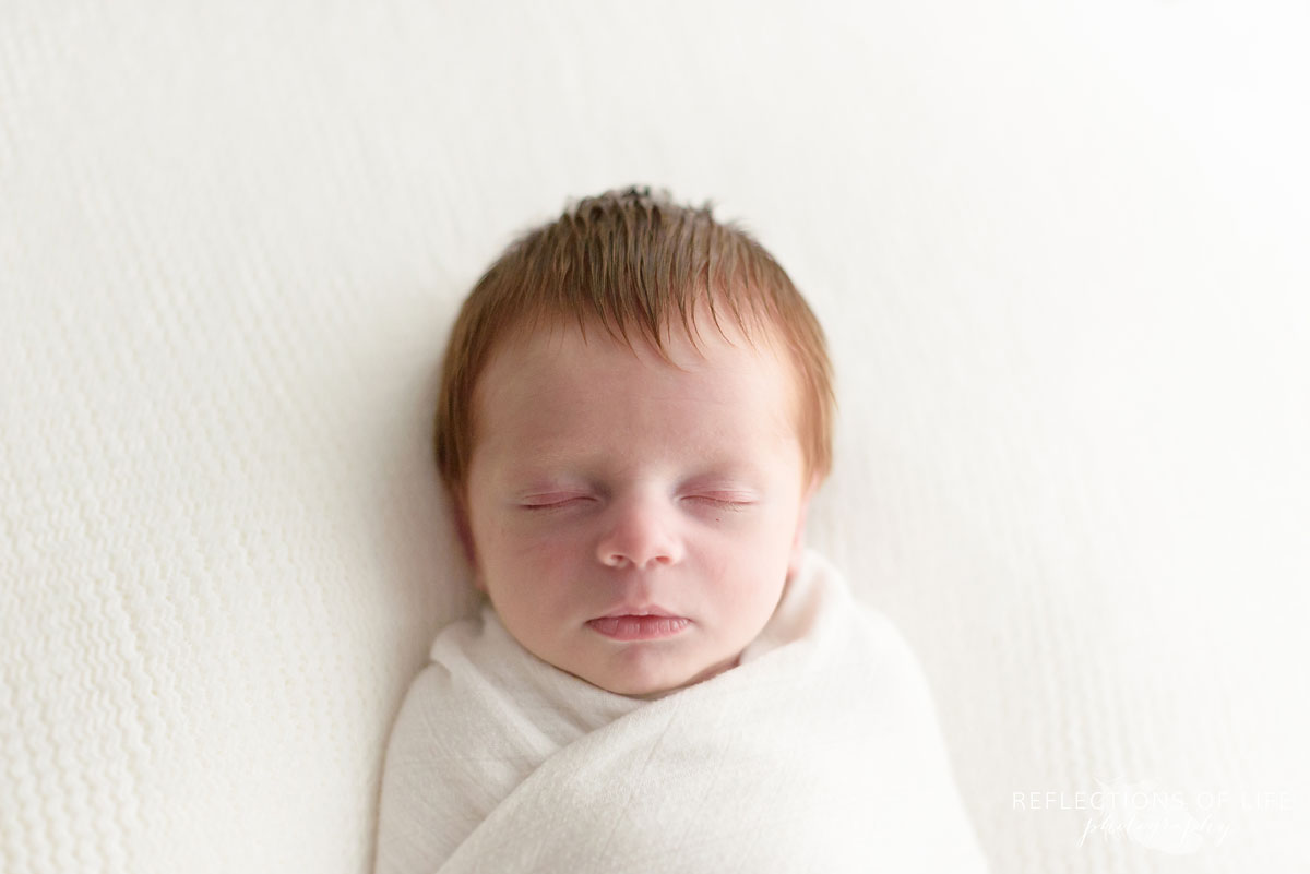 012 redhead newborn baby boy swaddled in white in Toronto photo studio