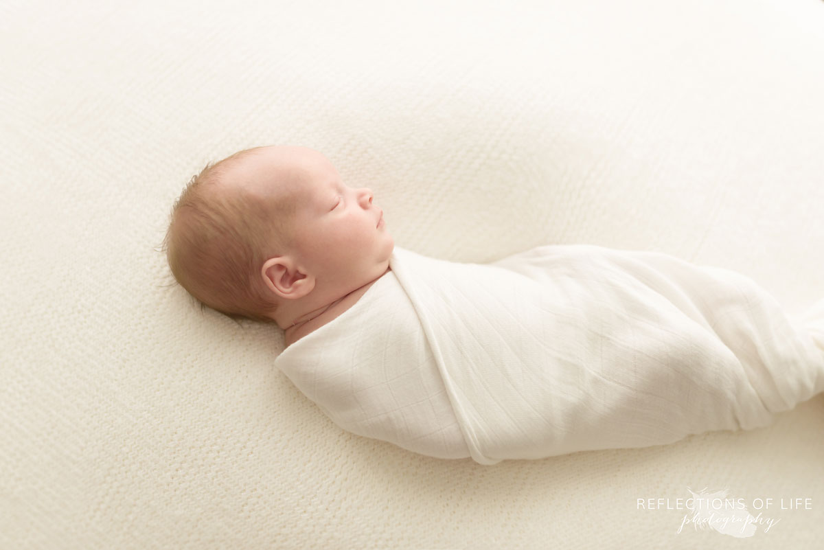 colour photo of newborn baby sleeping on beanbag swaddled in white blanket 002