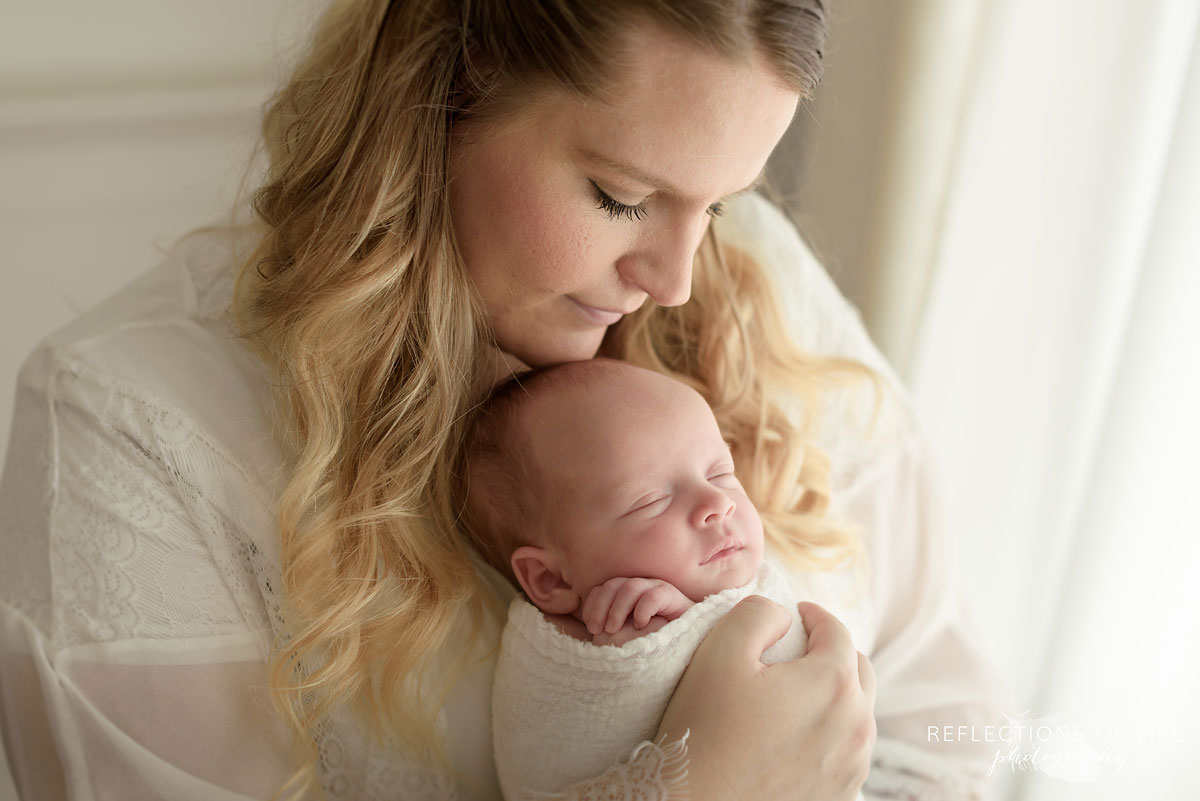 mommy and newborn baby boy snuggles by a window 016