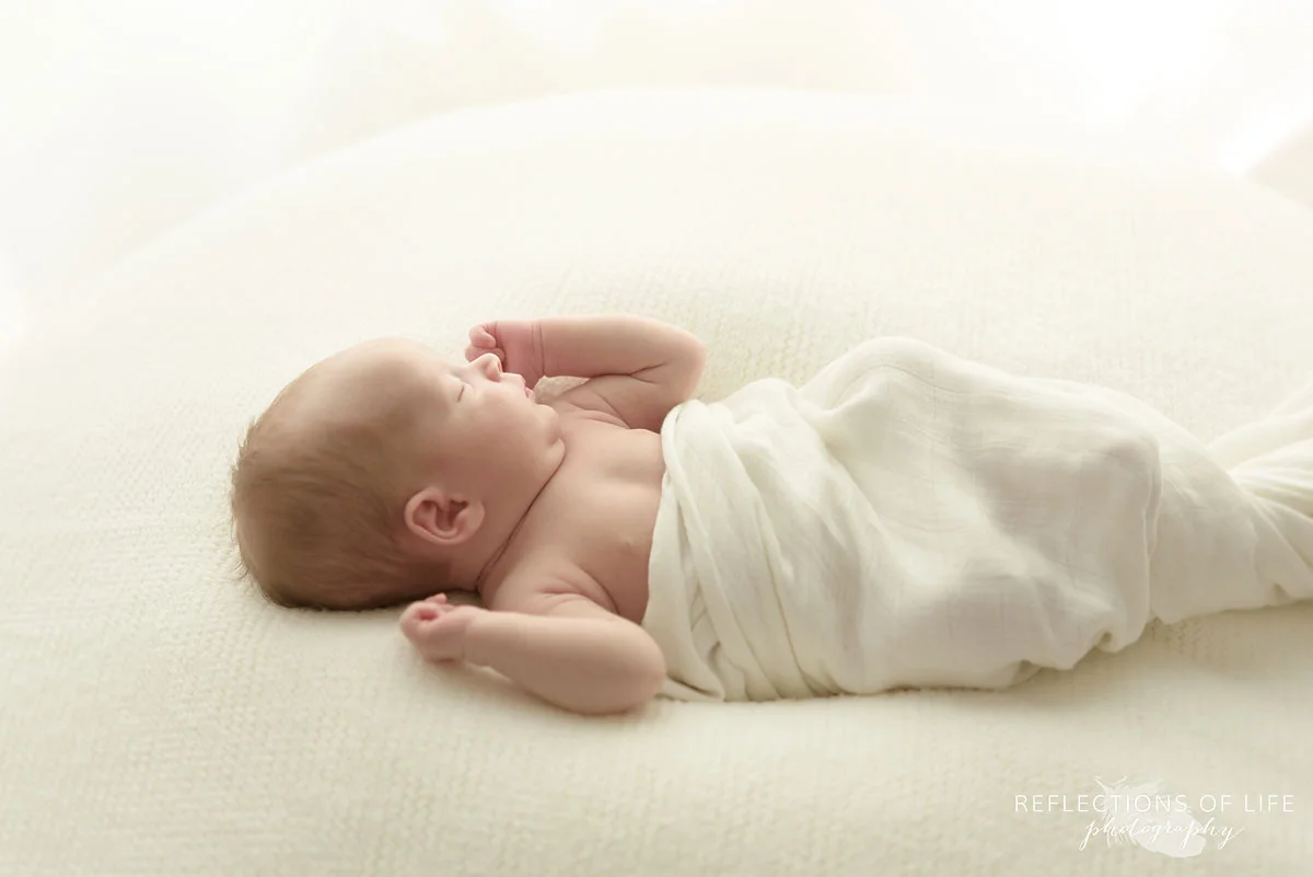 newborn baby swaddled in white on white blanket in natural light studio 008