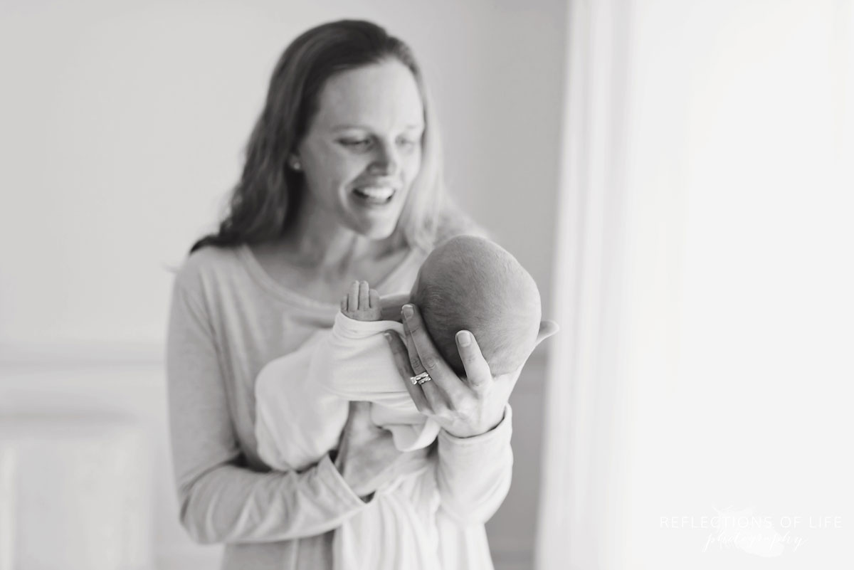 Adorable image of newborn in moms arms while she smiles