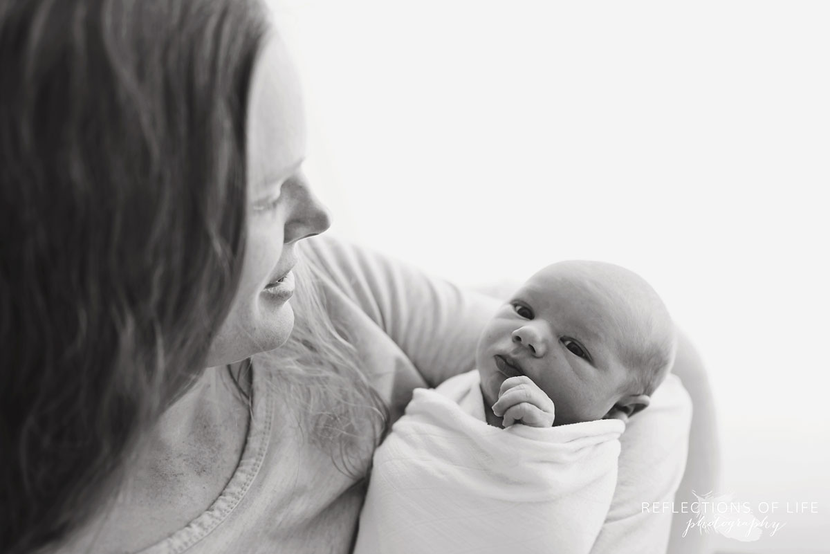 Black and white photo of mom with newborn baby swaddled in white little unicorm swaddle blanket