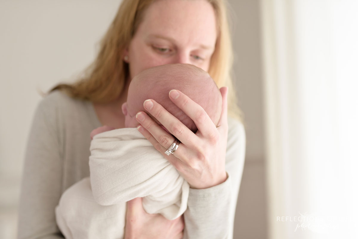 Mom leaning in and kissing her newborn baby in Niagara Newborn Photography studio