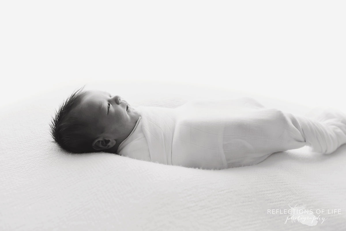 black and white of baby swaddled in white on bean bag in Niagara Region baby photo studio