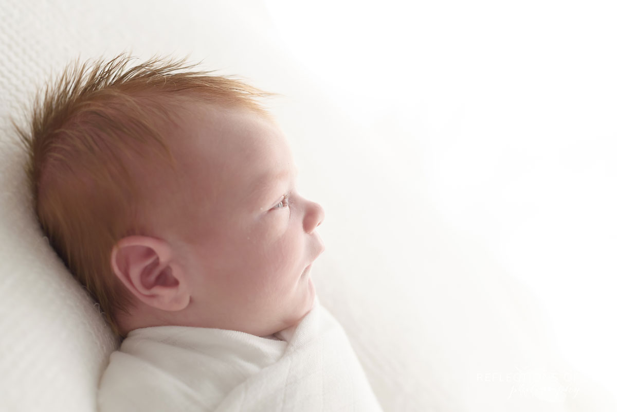 Side profile image of redhead newborn baby boy awake