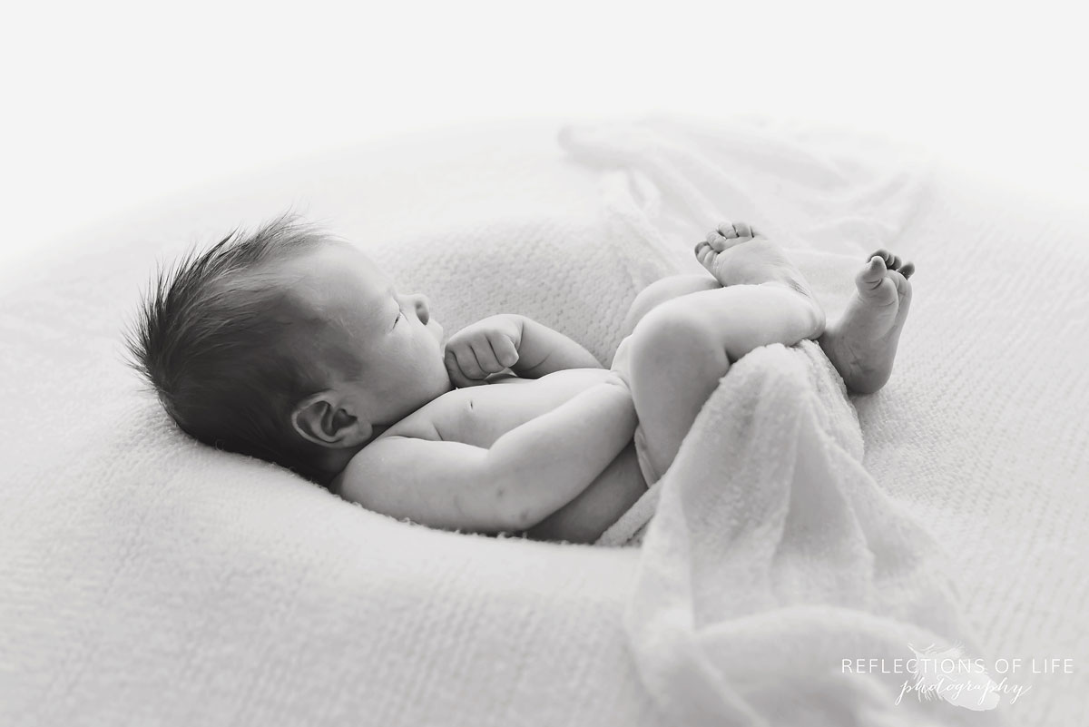 Adorable black and white image of baby boy relaxing on a cozy bean bag with white blanket