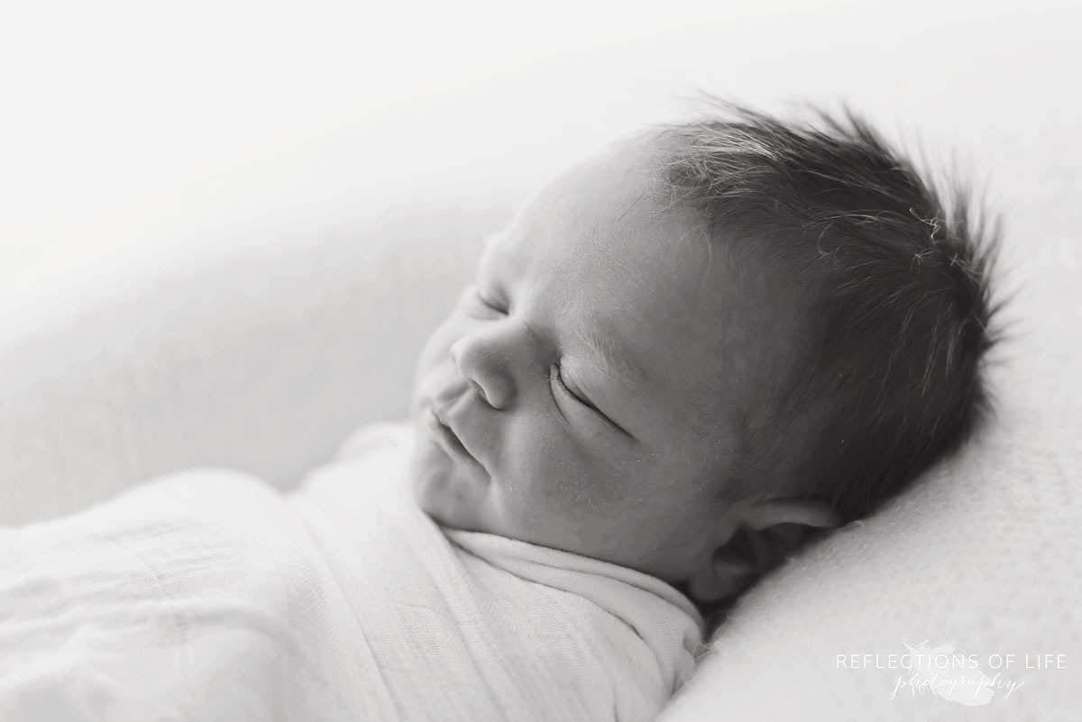 Black and white image of baby swaddled in white in natural light