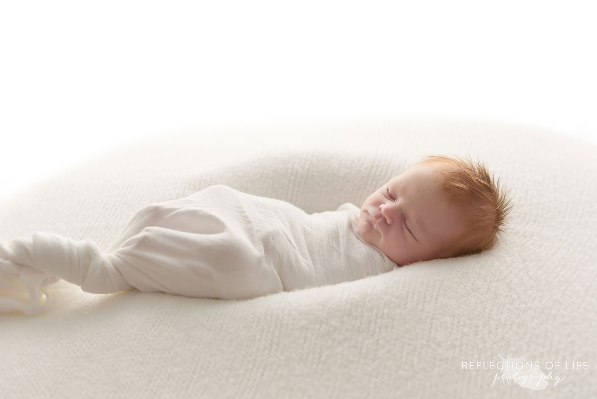 Natural light newborn baby photography of redhead swaddled in white