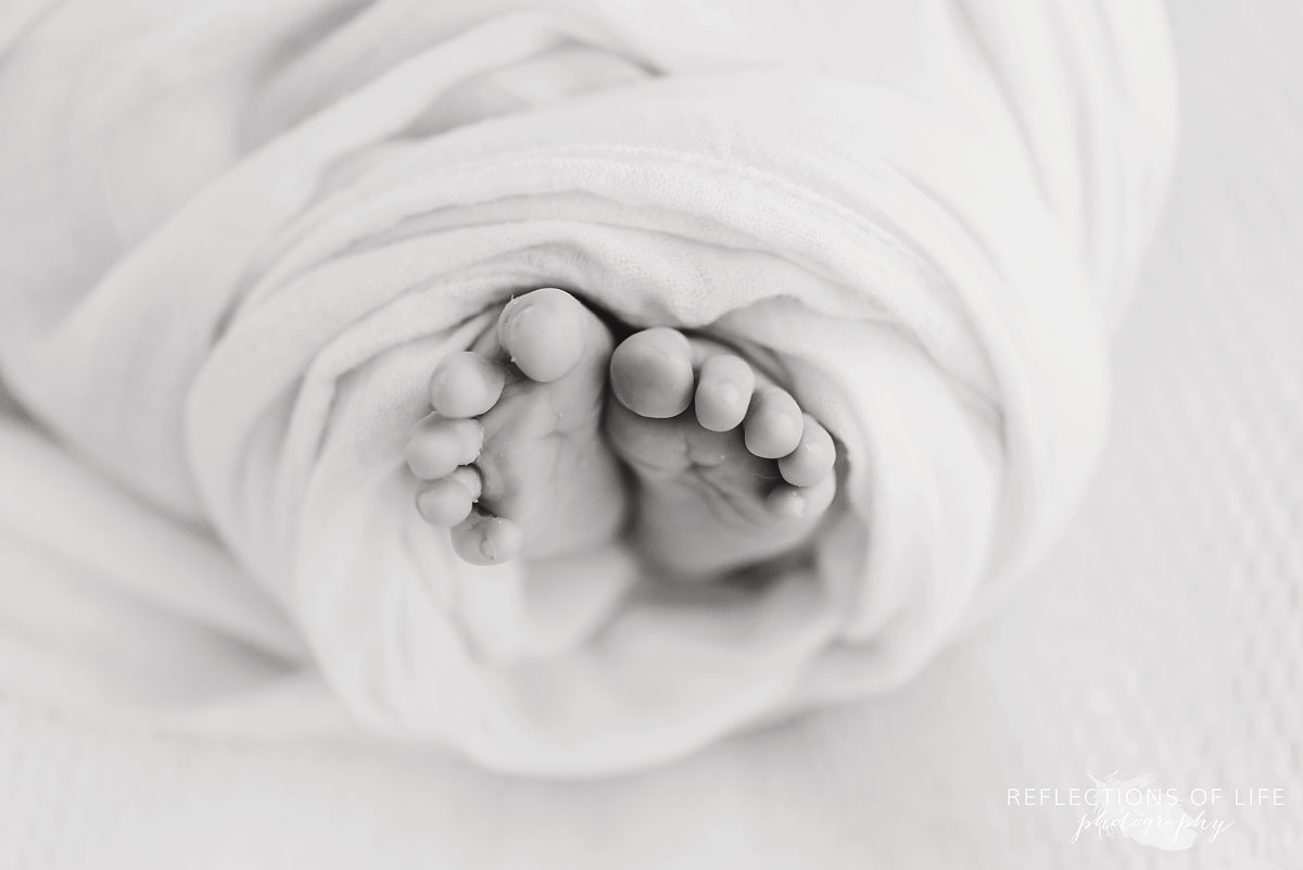 Black and white photo of newborn baby feet wrapped in Little Unicorn swaddle blanket