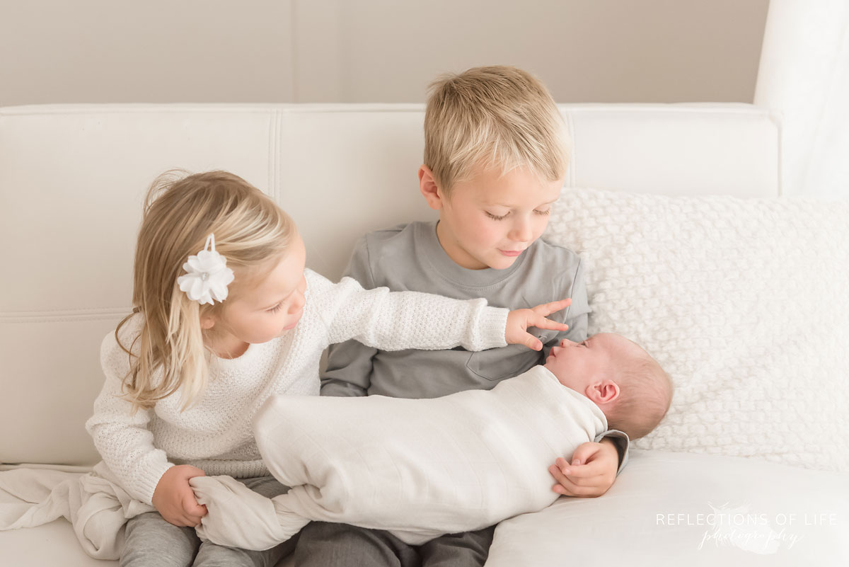 Family photo of siblings holding newborn baby sister