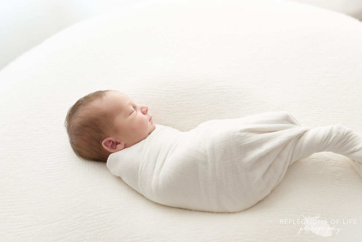 Colour photo of newborn baby swaddled in white on beanbag in Niagara Ontario Studio