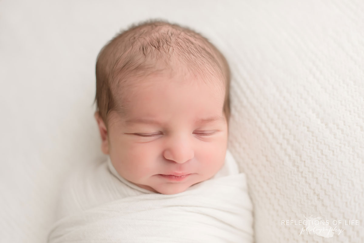 Newborn baby sleeping swaddled in white