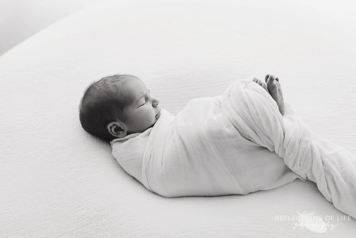 Black and white photo of newborn swaddled in white with his toes sticking out