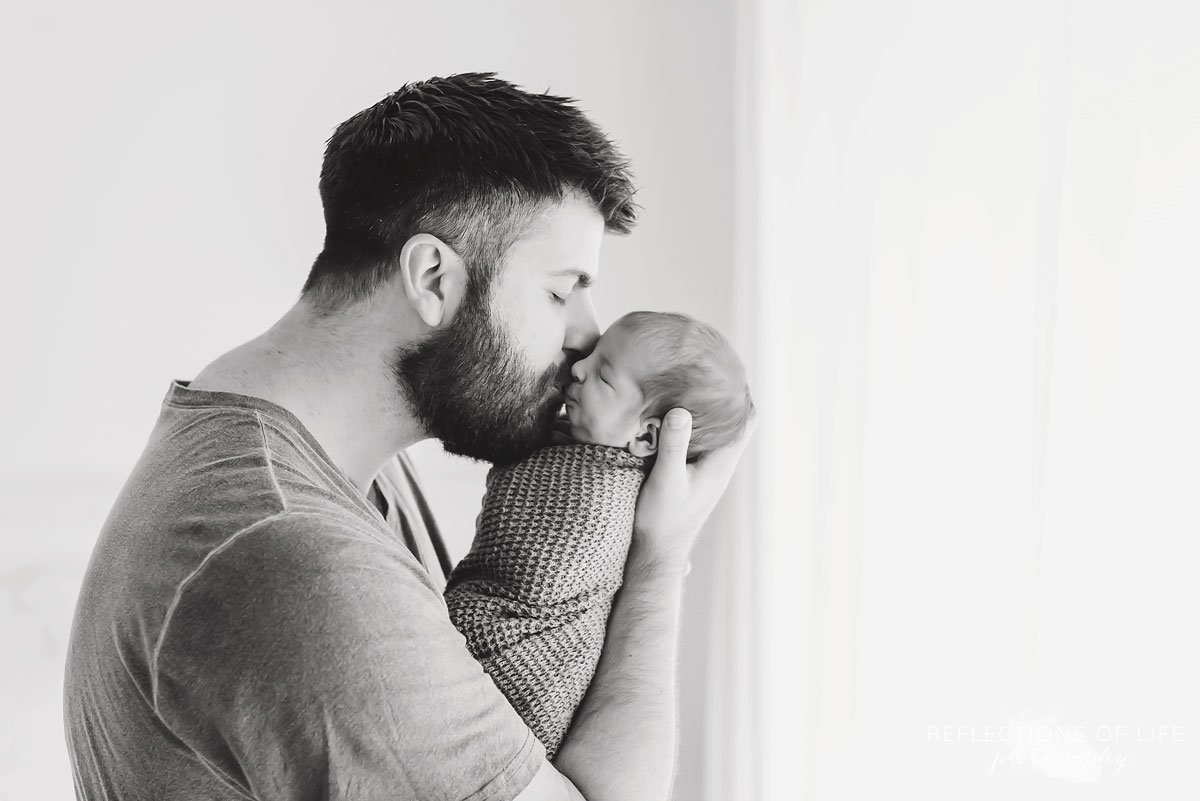 Black and white of daddy kissing newborn baby boy