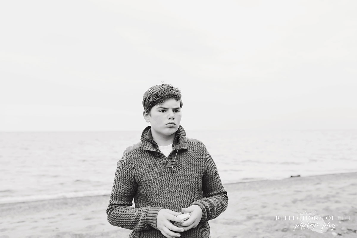 Teenage boy with a serious expression collecting rocks on the beach.jpg