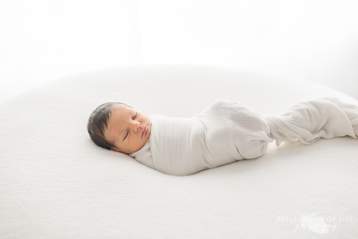Baby relaxing on a beanbag swaddled in white