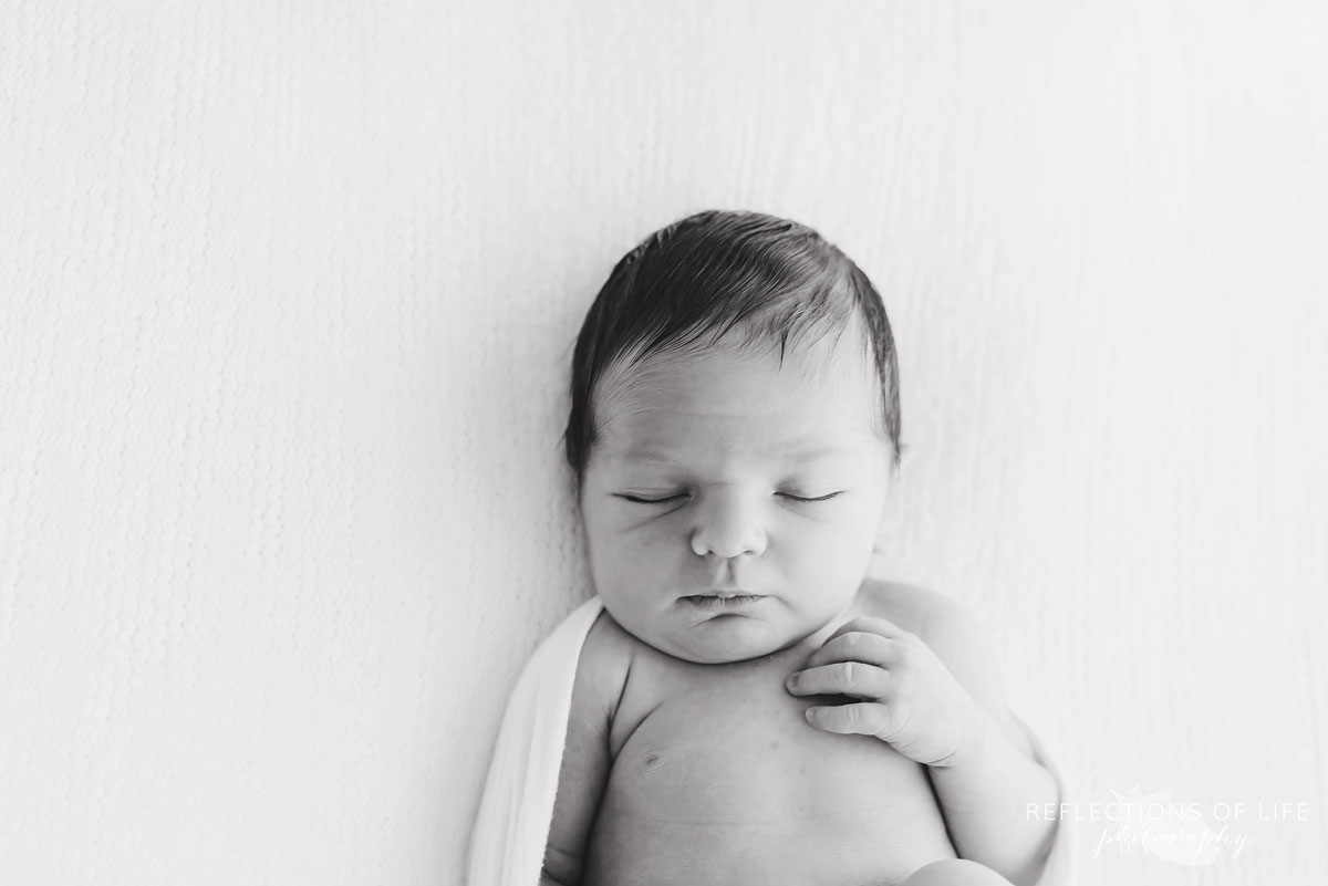 Black and white image of a baby relaxing on a white blanket