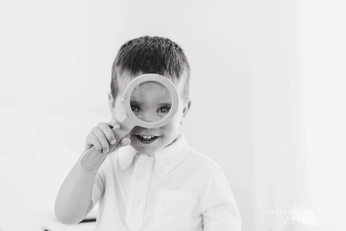 Black and white of little boy looking through a magnifying glass