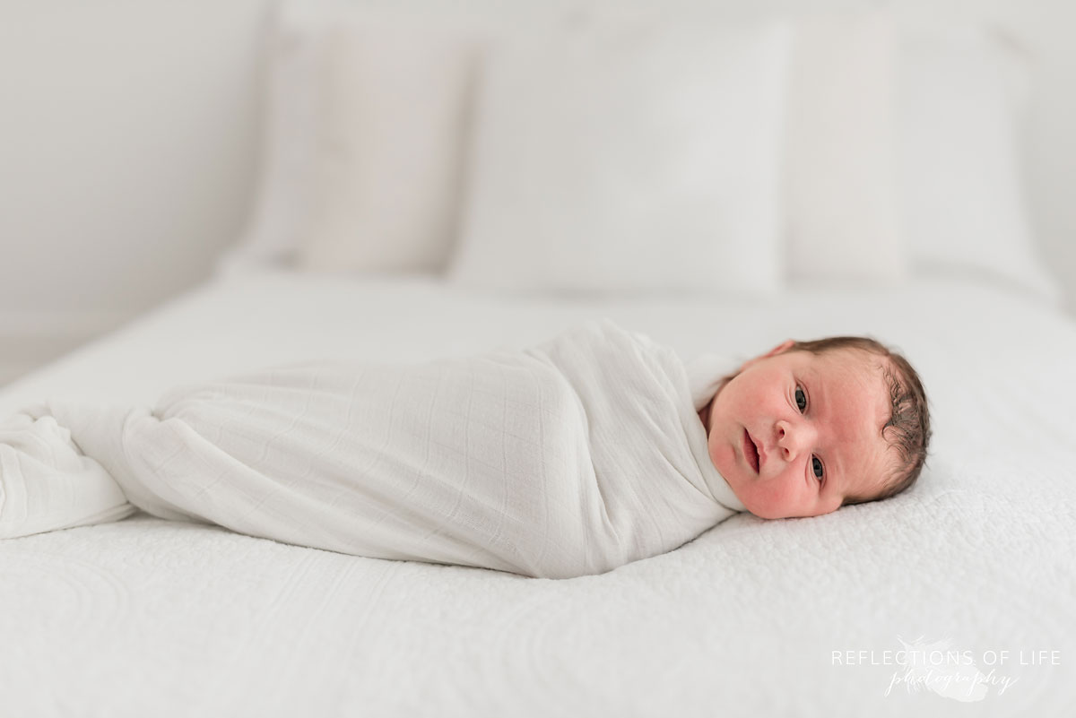 Natural light photography of newborn swaddled in white on white blankets