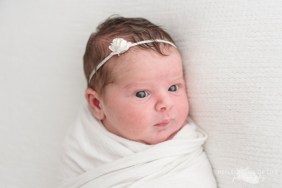 New born baby girl with white headband on white blanket