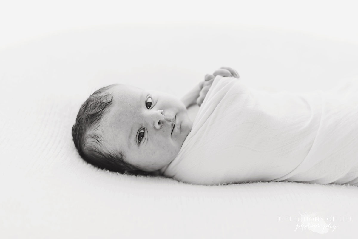 Black and white photo of  little newborn baby girl looking straight at the camera