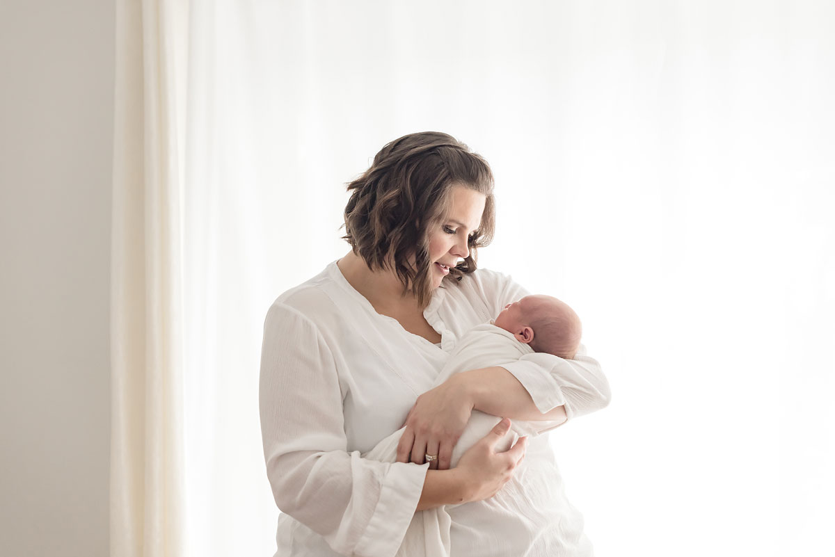 Beautiful backlit photograph of mother holding her newborn baby boy in front of a window