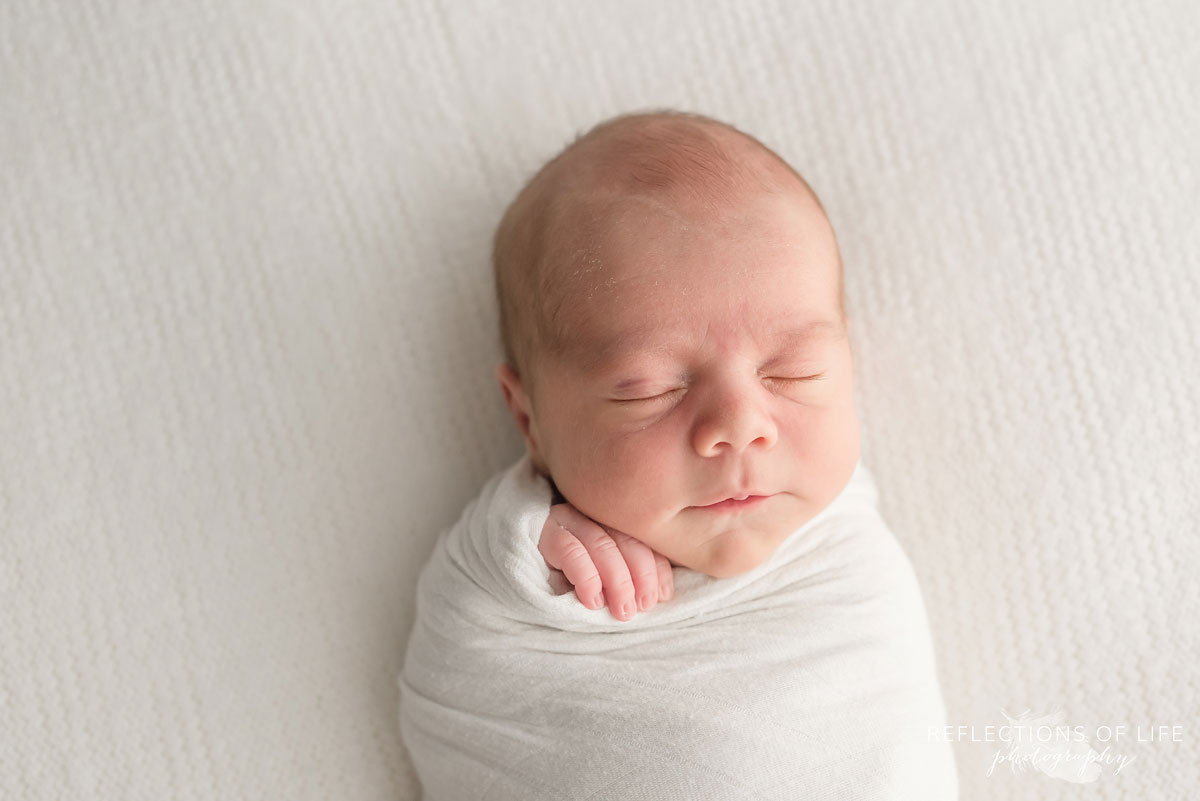 Newborn baby boy swaddled in white on a beanbag