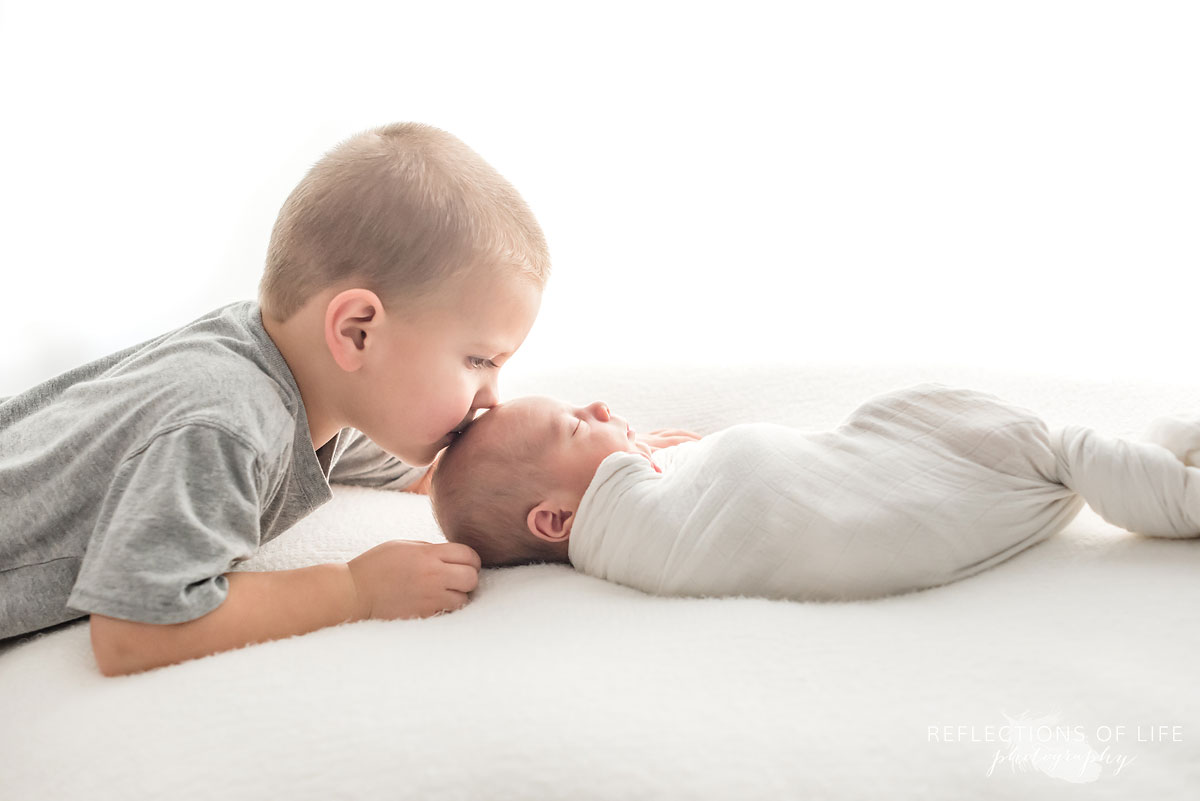Big brother giving his newborn baby brother a kiss on the head