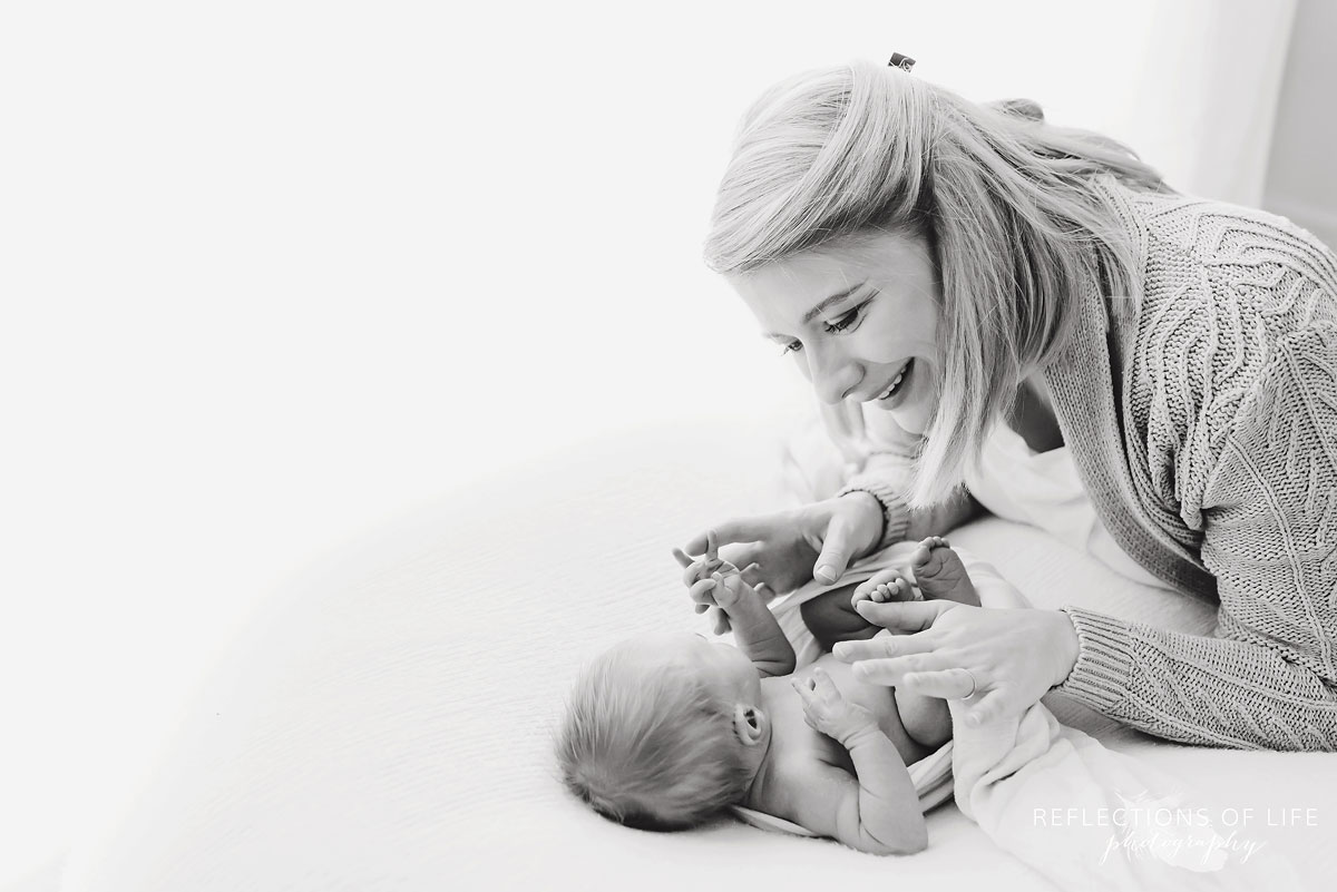 mother smiling at newborn child laying on bed black and white