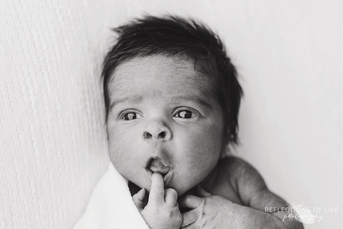 newborn baby sticking fingers in mouth black and white