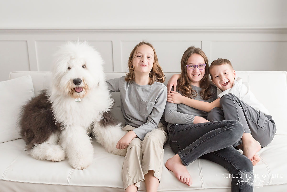 old english sheepdog sitting beside three happy smiling kids on couch