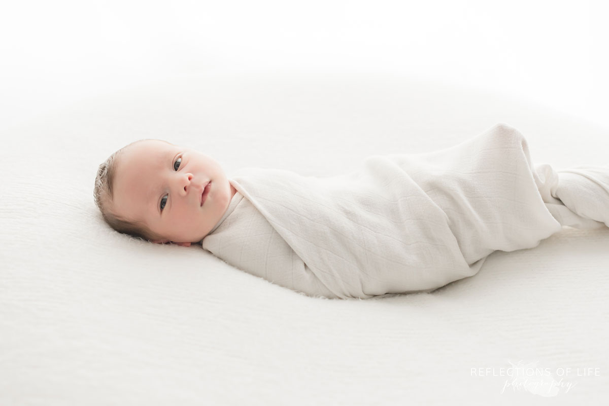 young baby boy newborn swaddled looking at camera