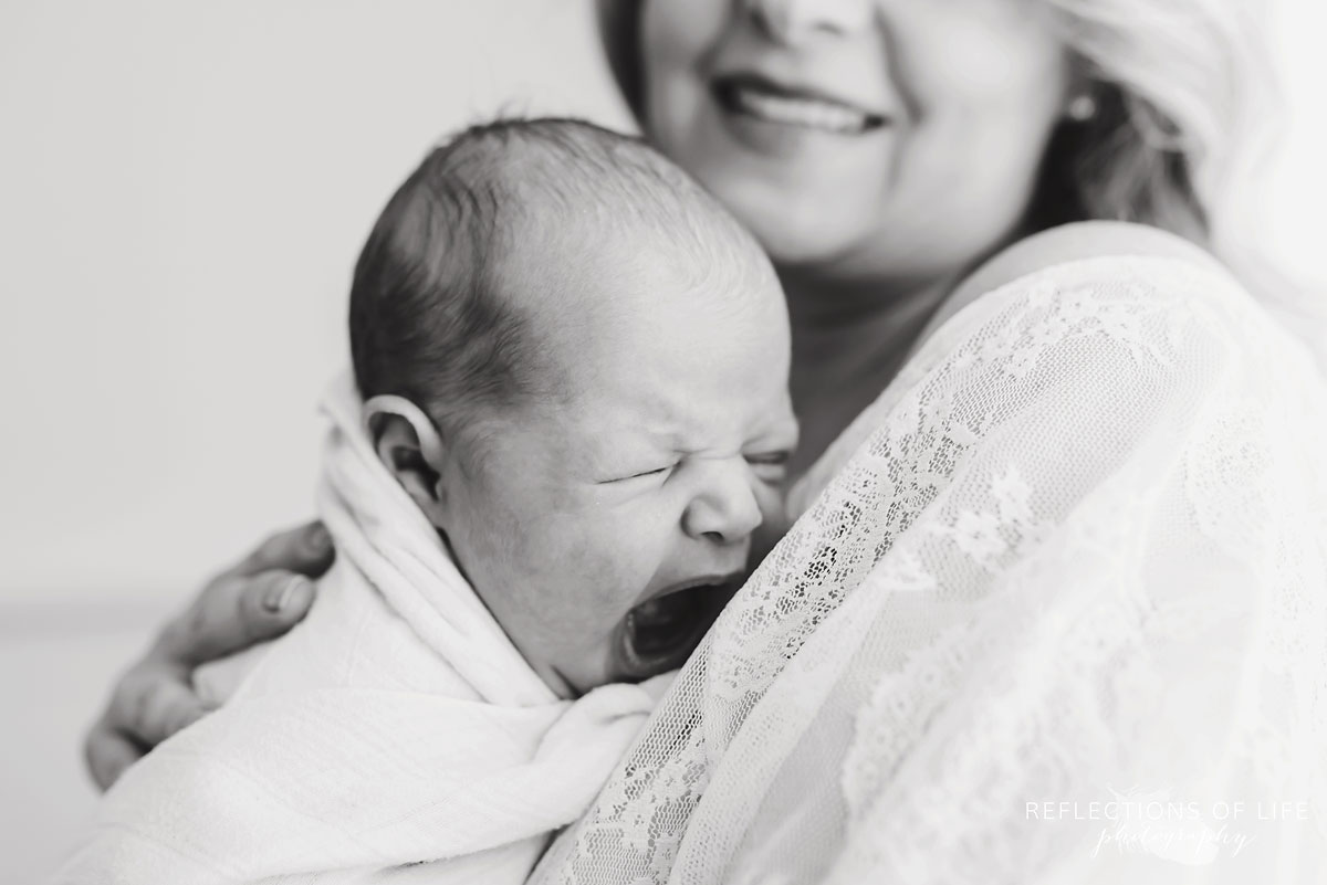 mother holding yawning newborn baby in arms black and white