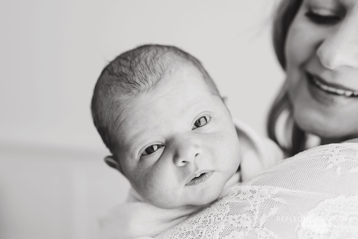 newborn baby in mothers arms looking into camera black and white