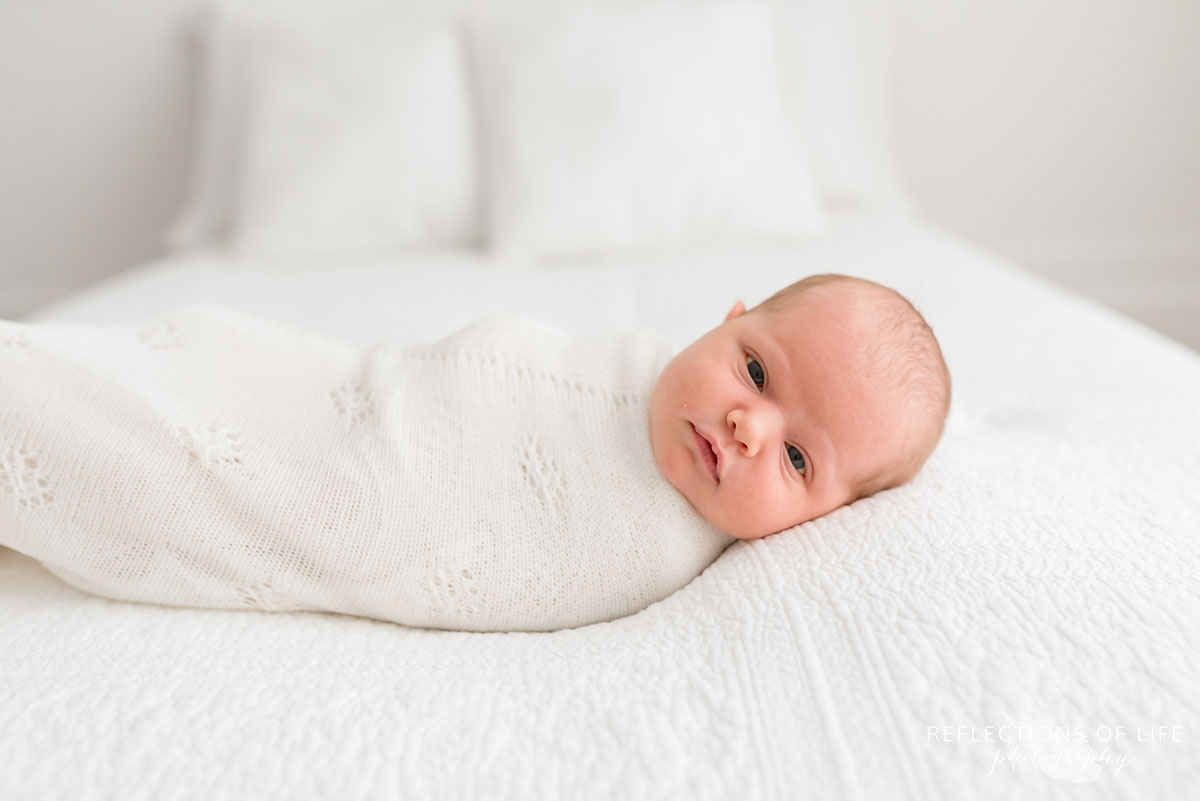 newborn baby girl laying on bed looking into cameranewborn baby girl laying on bed looking into camera