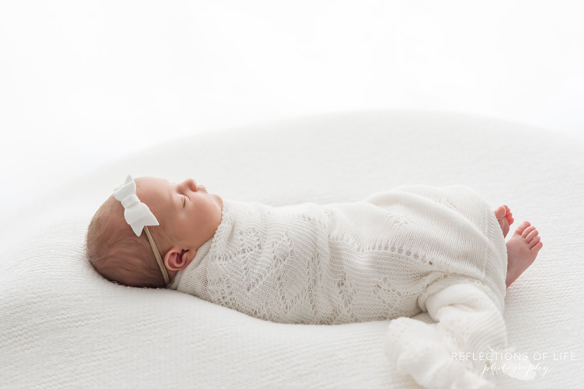 newborn baby laying on bed wearing headband