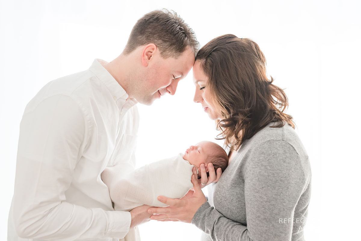 parents rest their heads together breathing in that new baby smell of their newborn