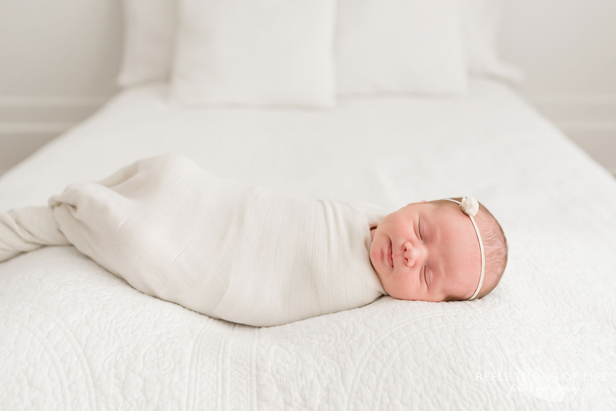 newborn baby girl with white headband sleeping on white bed