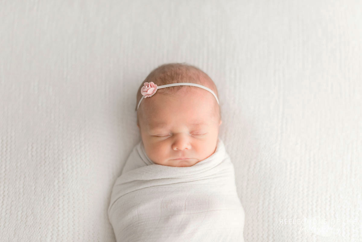 Little newborn bby girl swaddled in little white unicorn blanket with small rose headband