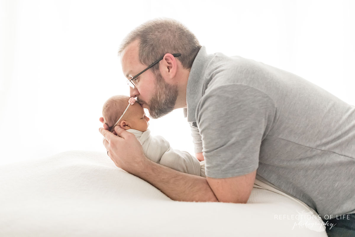 New dad kissing baby girl on white beanbag in natural light