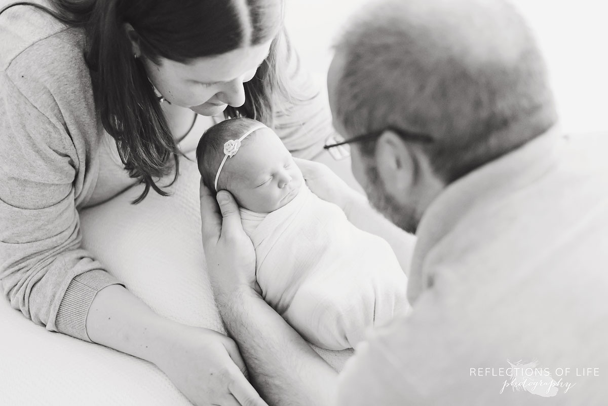 newborn baby girl in the arms of her dad with mom overlooking
