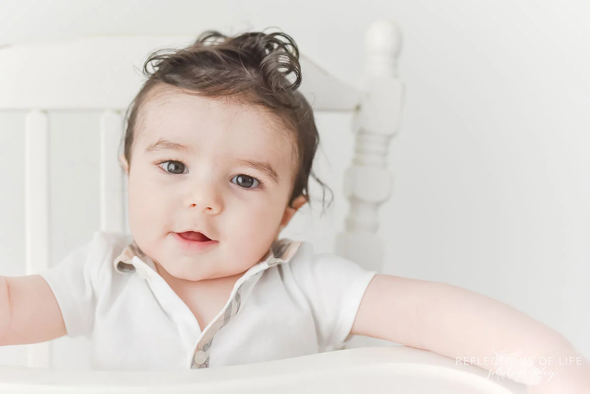 baby boy sitting in an antique white high chair smiling at the camera.jpg